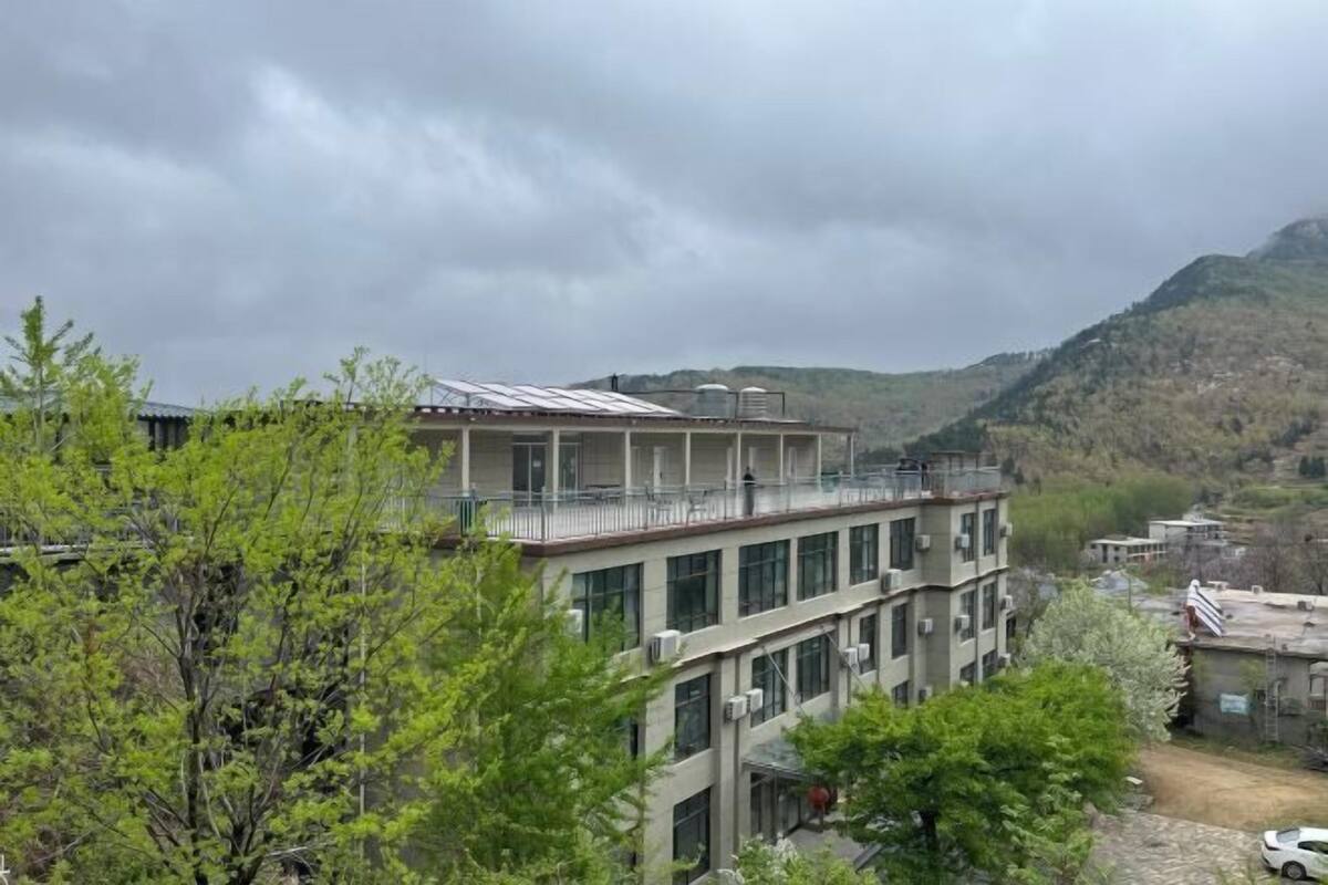 Un edificio de varios pisos con balcones, rodeado de follaje y montañas.
