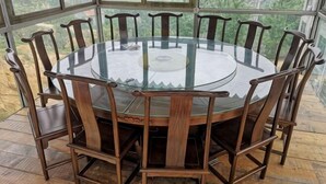 A round glass table with wooden chairs, surrounded by large windows offering a view of greenery. - Monkey Mountain Villa Hotel (Mengyin)
