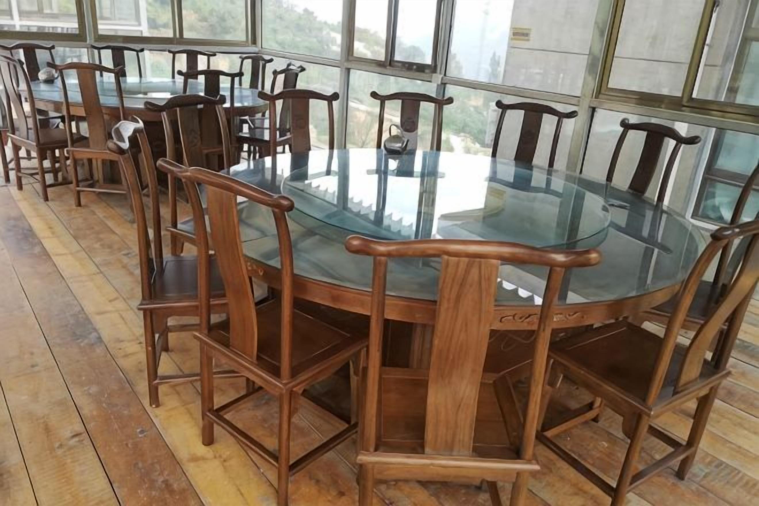 A round glass table surrounded by wooden chairs in a room with large windows.