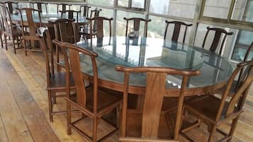 A round glass table surrounded by wooden chairs in a room with large windows.