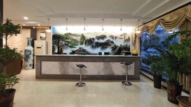 Un área de recepción con mostrador de mármol, dos taburetes de bar, un mural grande de un paisaje y plantas en macetas.