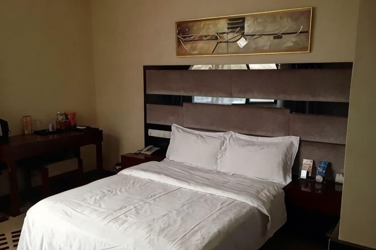 A hotel room with a large bed, a nightstand, a desk, and a painting on the wall.