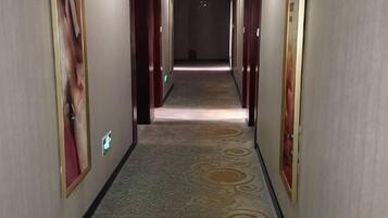 A hallway with patterned carpet, doors on either side, and a light source at the end.