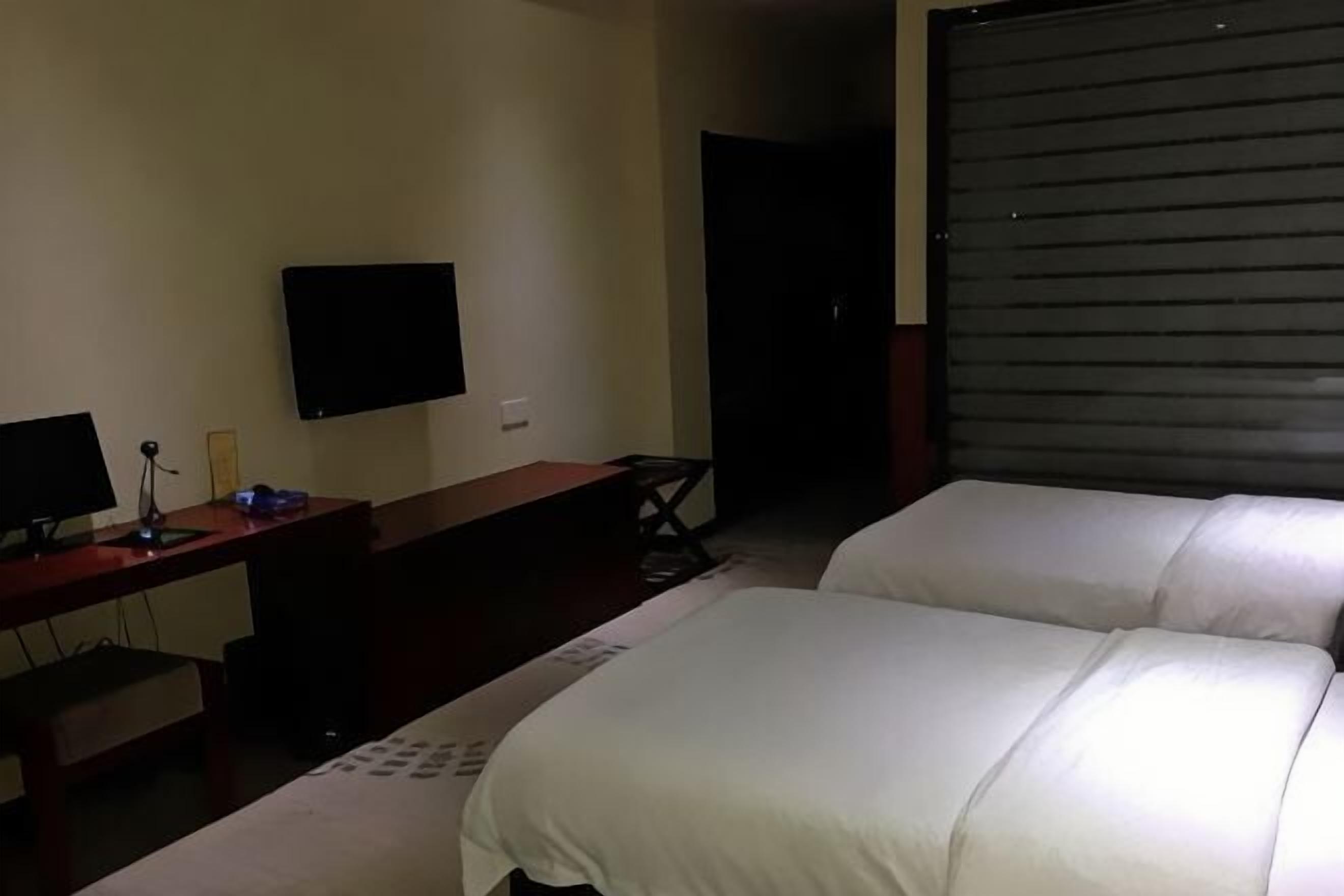 Una habitación de hotel con una cama, un escritorio con una computadora, un televisor y una puerta corredera cerrada.