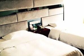 A hotel room with two beds, a nightstand with a lamp, and a mirror. - Tiantian Holiday Hotel (Tongcheng)