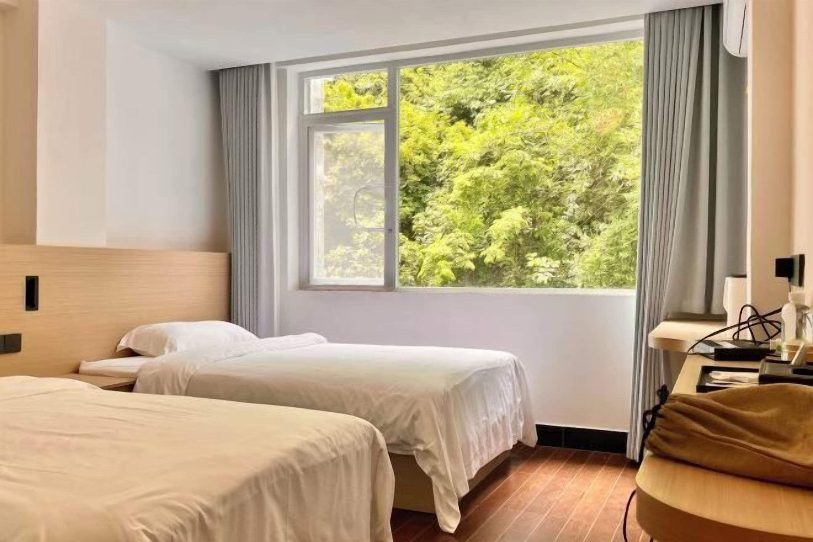 Habitación de hotel con dos camas, un escritorio, una silla y ventana con vistas a zonas verdes.