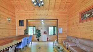 Interior de madera con zona de comedor, un sofá, una lámpara de araña y un cuadro en la pared.