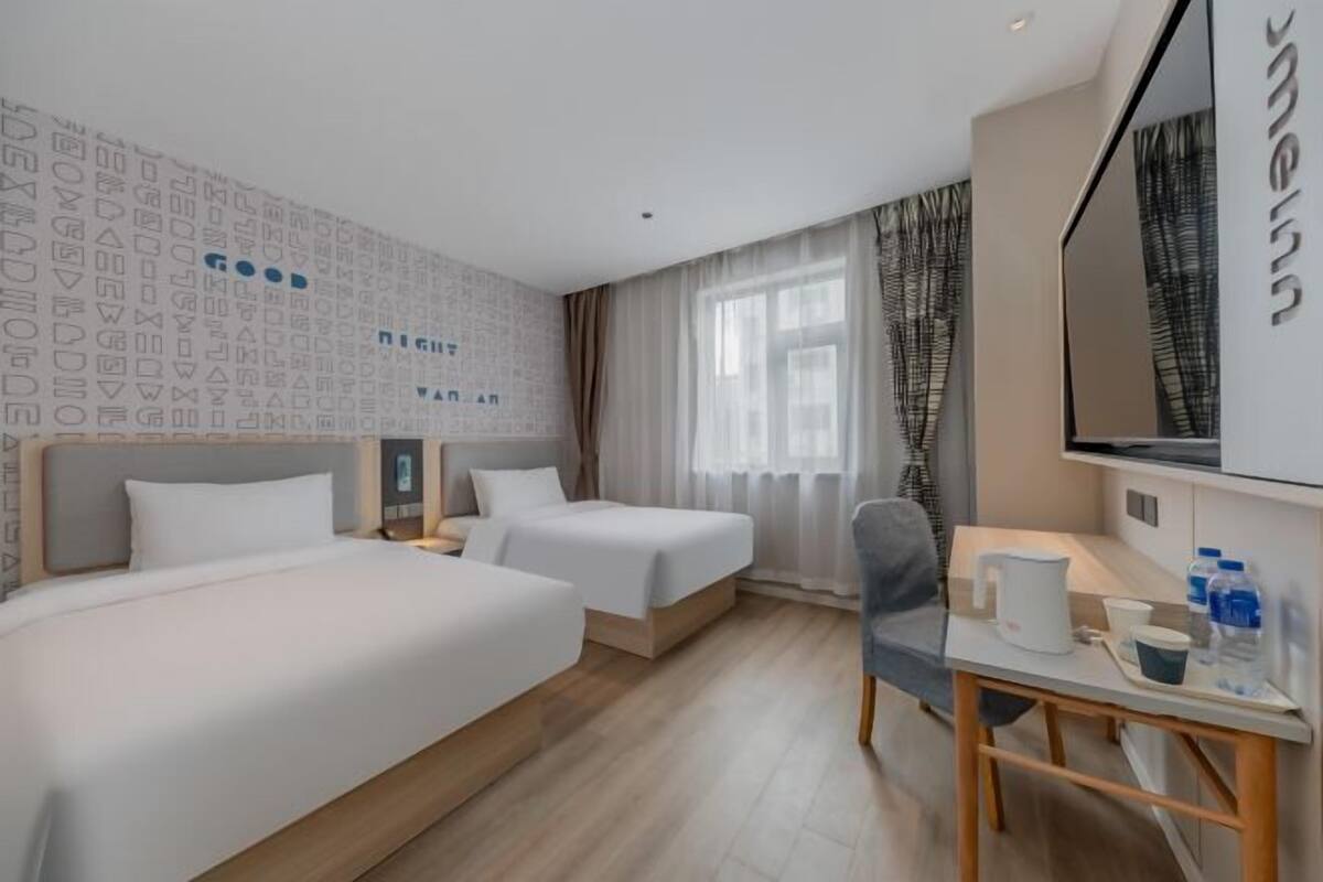 A hotel room with two beds, a desk, a chair, a TV, and a window with curtains.