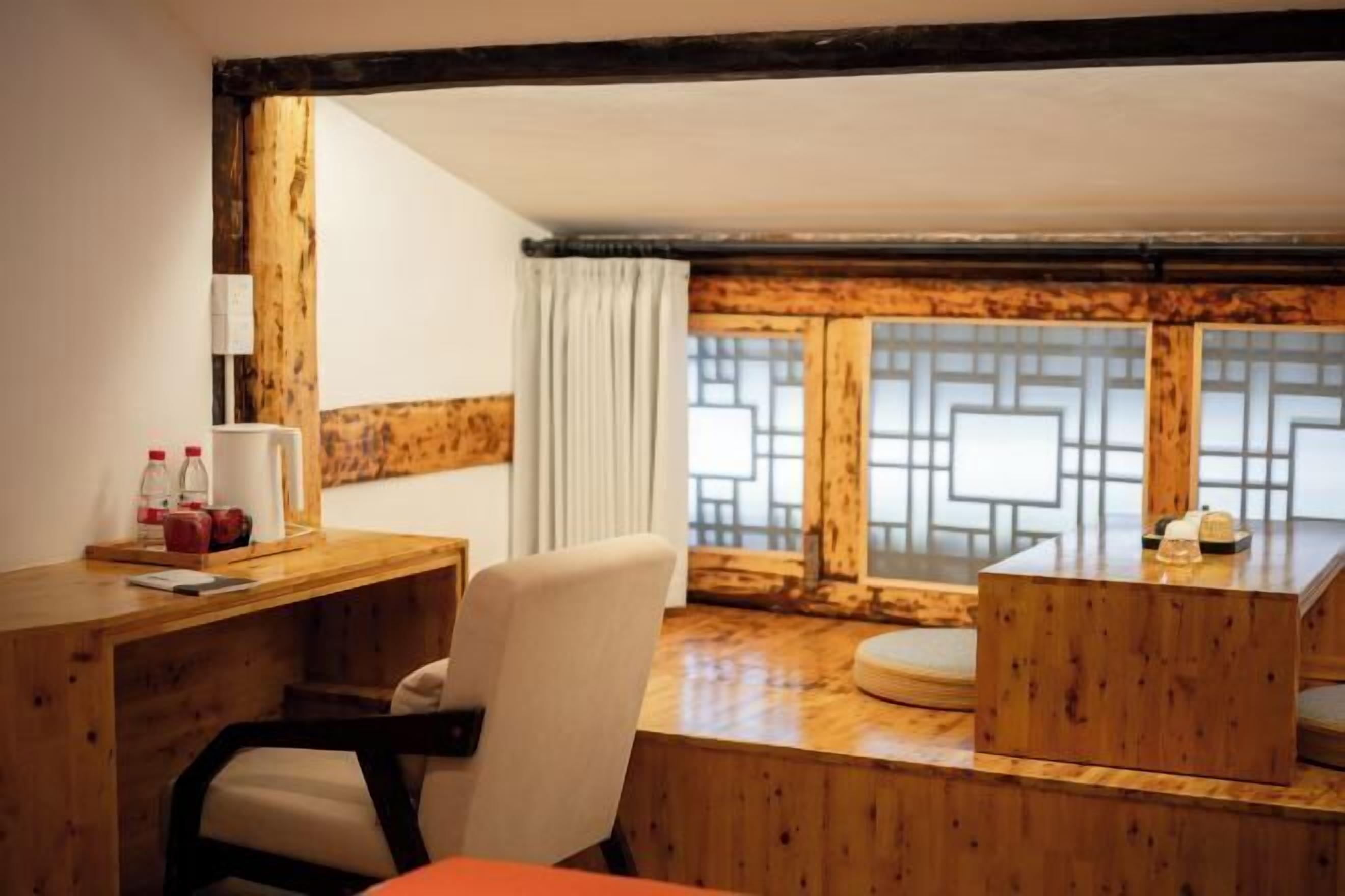 Une pièce meublée de meubles en bois, avec un bureau, une chaise et une fenêtre ornée d’un motif géométrique.