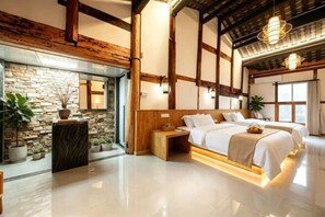 A bedroom with a stone wall, wooden beams, a large bed, bedside tables, and a hanging light fixture.
