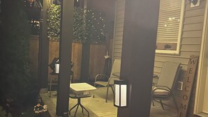 A covered outdoor patio with string lights, a welcome sign, and a small table with chairs. - Quiet Private suite in a forest setting w/Parking and AC | Maple Ridge (Maple Ridge)