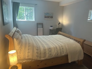 Un dormitorio con una cama, una mesita de noche, una lámpara, una ventana, un cartel y una silla.