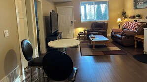 A living room with a brown leather chair, a sofa, a television, and a window with blinds. - Quiet Private suite in a forest setting w/Parking and AC | Maple Ridge (Maple Ridge)