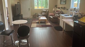 A living room with a sofa, chairs, a coffee table, a TV, and a kitchen area with a sink and stove. - Quiet Private suite in a forest setting w/Parking and AC | Maple Ridge (Maple Ridge)