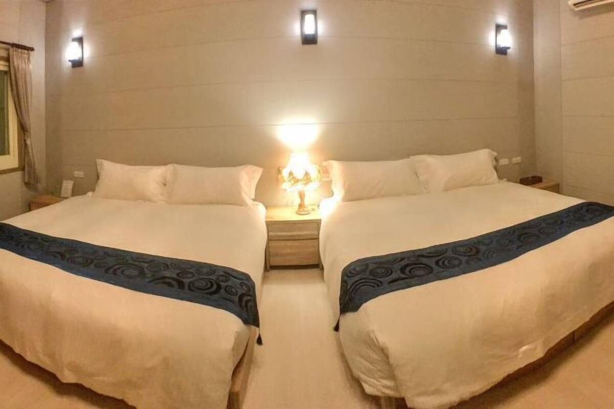 Een hotelkamer met twee bedden, een nachtkastje met een lamp en een wandlamp.
