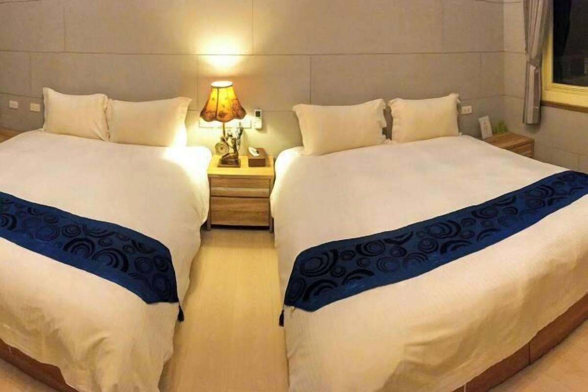 Een tweepersoonsbed met een blauwe spreidek, een nachtkastje met een lamp en een nachtkastje met een telefoon.