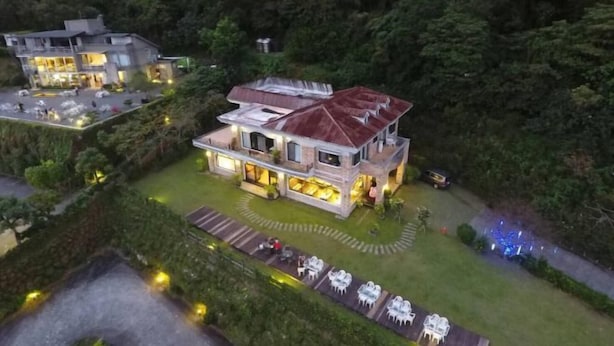 A large, two-story house with a spacious patio area and multiple outdoor seating arrangements.