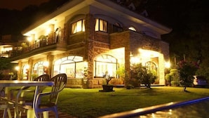 A two-story house with a balcony, a well-lit front entrance, and a lawn.