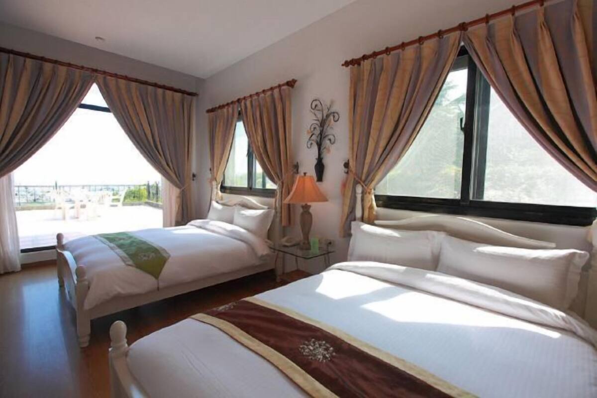 Een hotelkamer met twee bedden, een lamp, gordijnen en uitzicht op de omgeving.