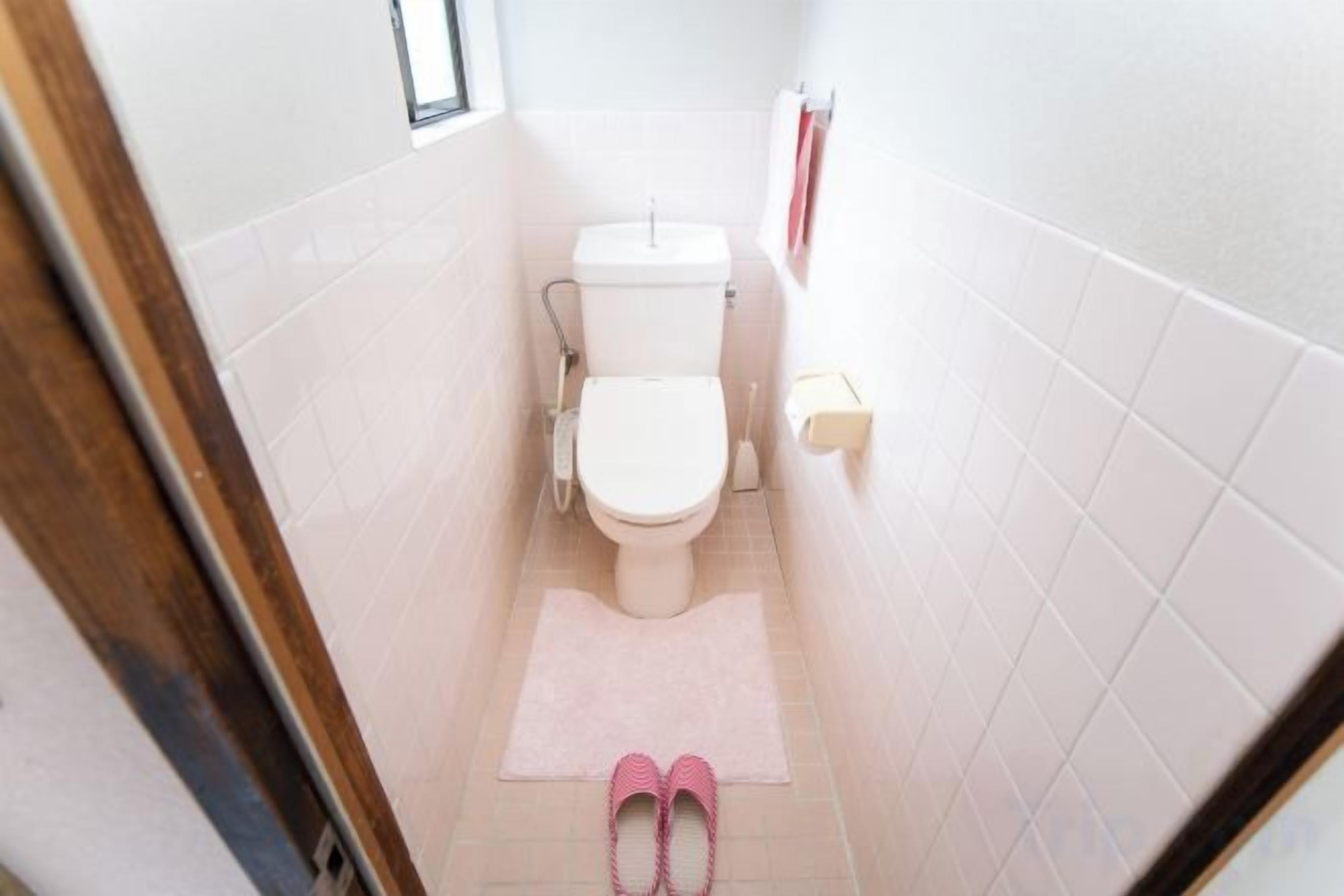 A bathroom with a toilet, a small window, and a pink mat on the floor.