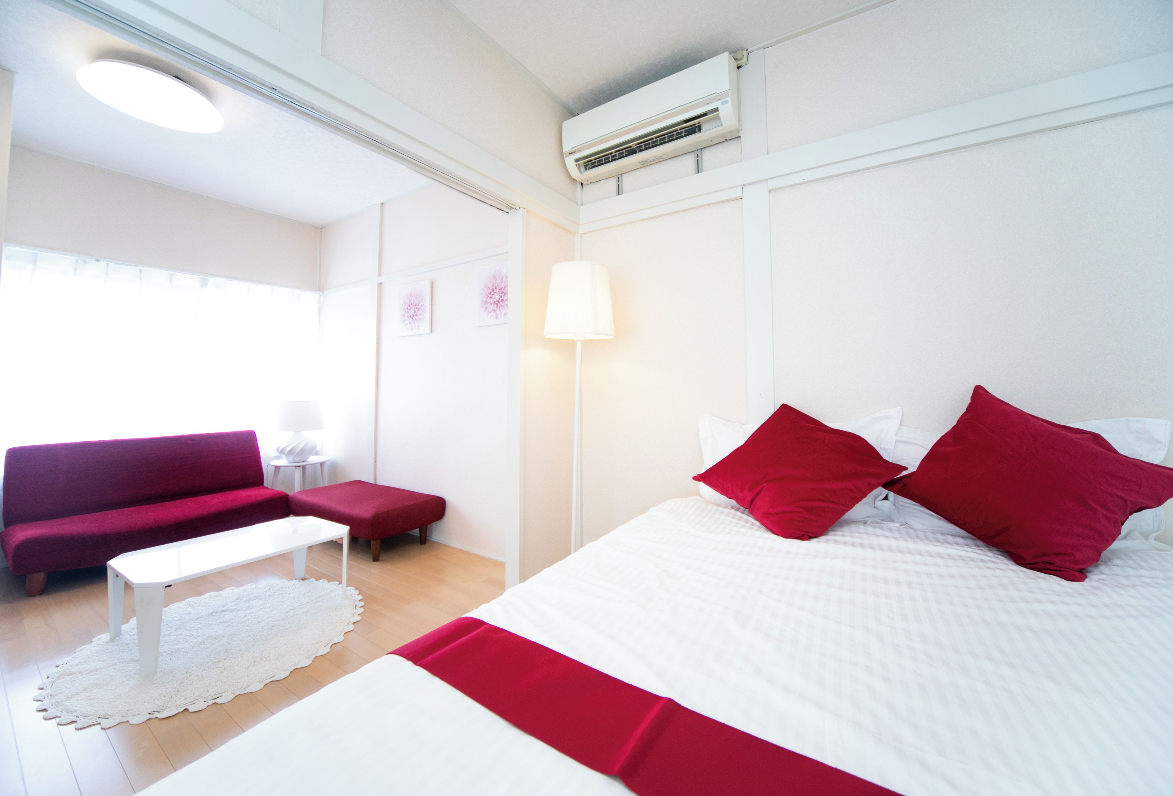 Una habitación de hotel con una cama, un sofá rojo, una mesa blanca y una lámpara blanca.