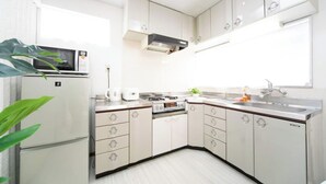 A modern kitchen with white cabinets, a microwave, a stove, and a sink. - Yokkaichi Nishishinchi Hotel (Yokkaichi)