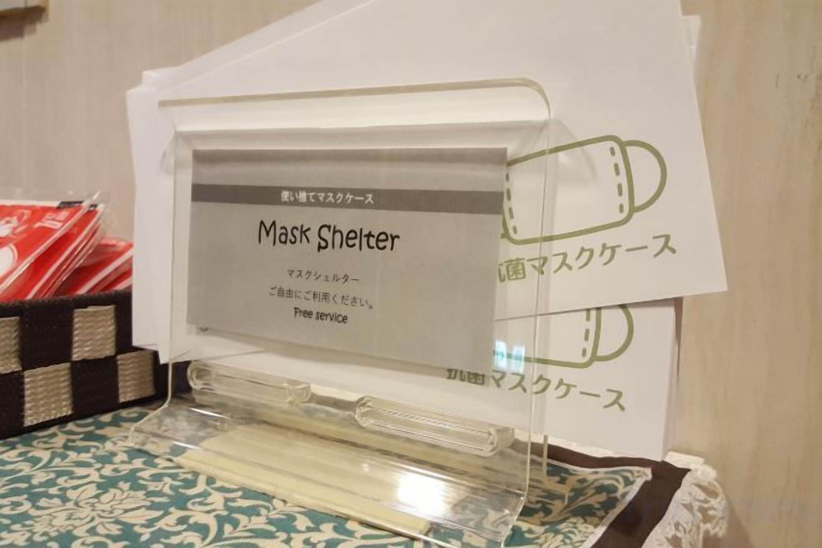 Ein Verkaufsständer mit einem Schild für den Service 'Mask Shelter', ausgestattet mit einer klaren Schutzhülle und weißem Hintergrund.