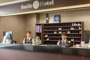 A reception desk at Smile Hotel with a counter, a computer, and a shelf with cups. - Smile Hotel Kushiro (Kushiro City)