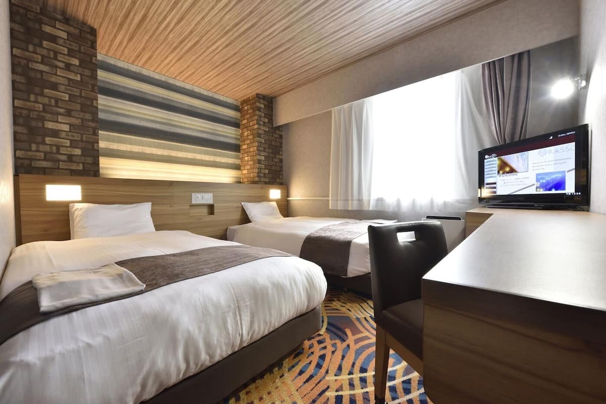 Hotellihuone, jossa on kaksi sänkyä, työpöytä, televisio ja kuviollinen matto.