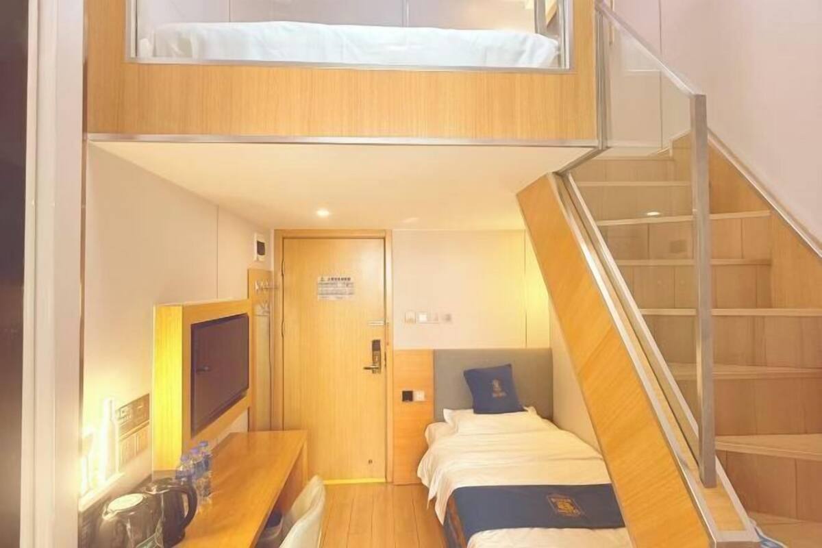 A compact hotel room with a bunk bed, a small desk with a chair, a television, and a staircase.