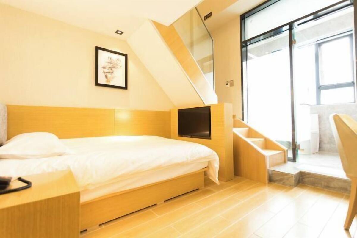 A modern bedroom with a bed, a TV, a staircase, and a large window.