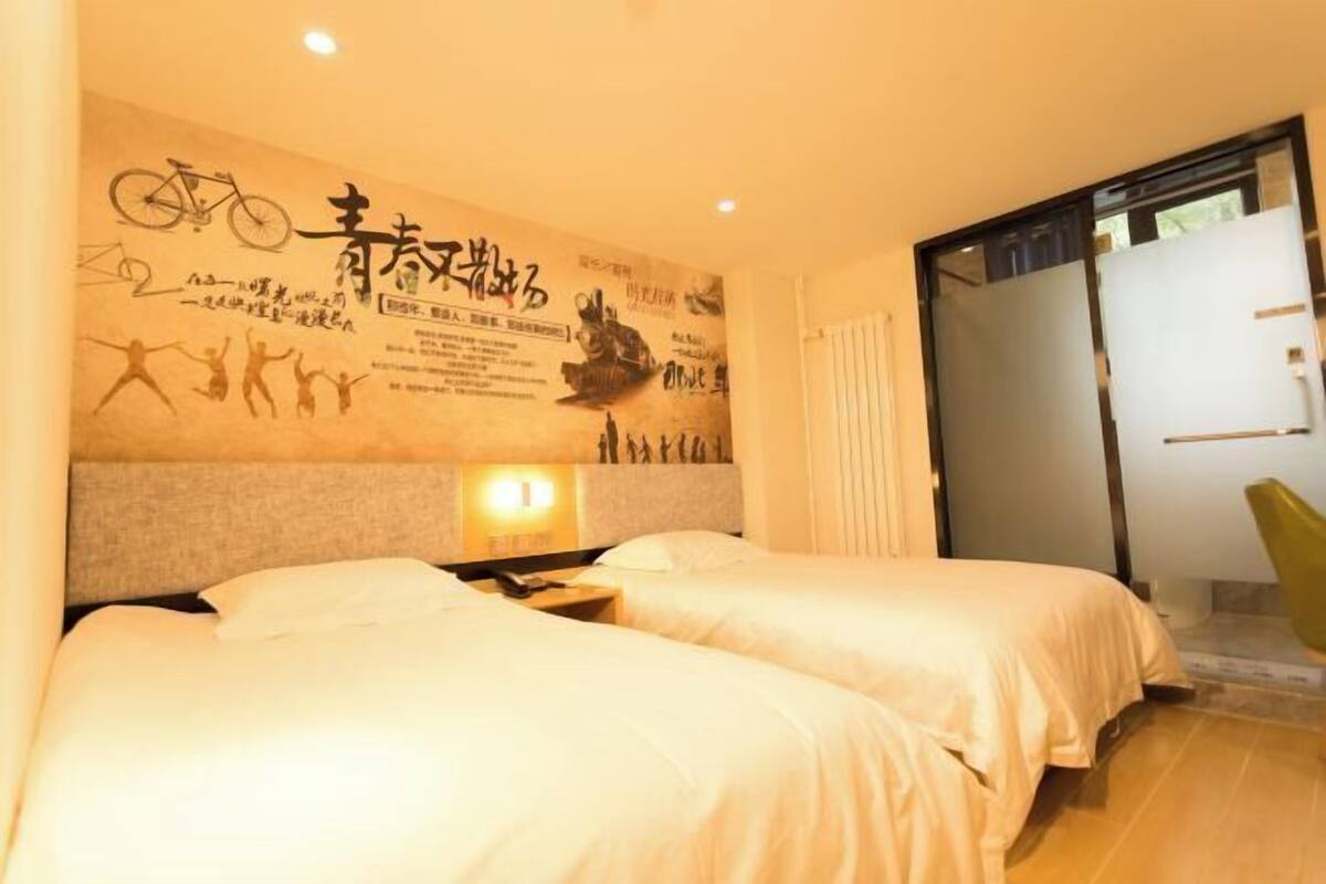 A hotel room with two beds, a wall with various decorations, a nightstand, and a sliding door to the right.