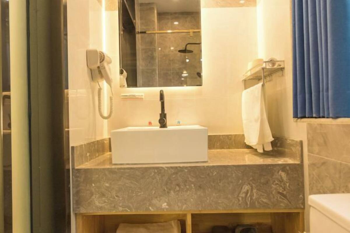 A bathroom with a marble countertop, a sink, a mirror, a shower, and a towel rack.