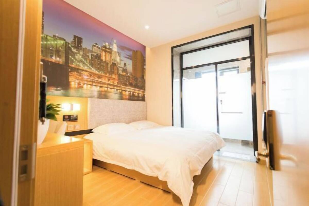A hotel room with a bed, a nightstand, a wall-mounted TV, and a cityscape mural.
