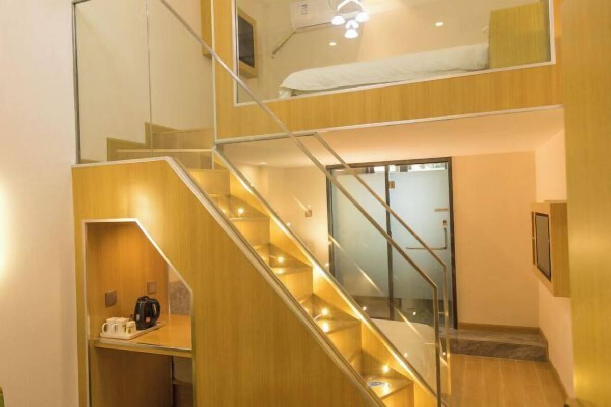 A multi-level interior with a staircase, a bed on the upper level, and a coffee machine on the lower level.