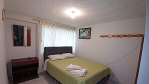 A small, clean room with a single bed, a bedside table, and a window with curtains.