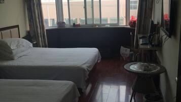 A hotel room with two beds, a small table, and a window with a view of buildings.