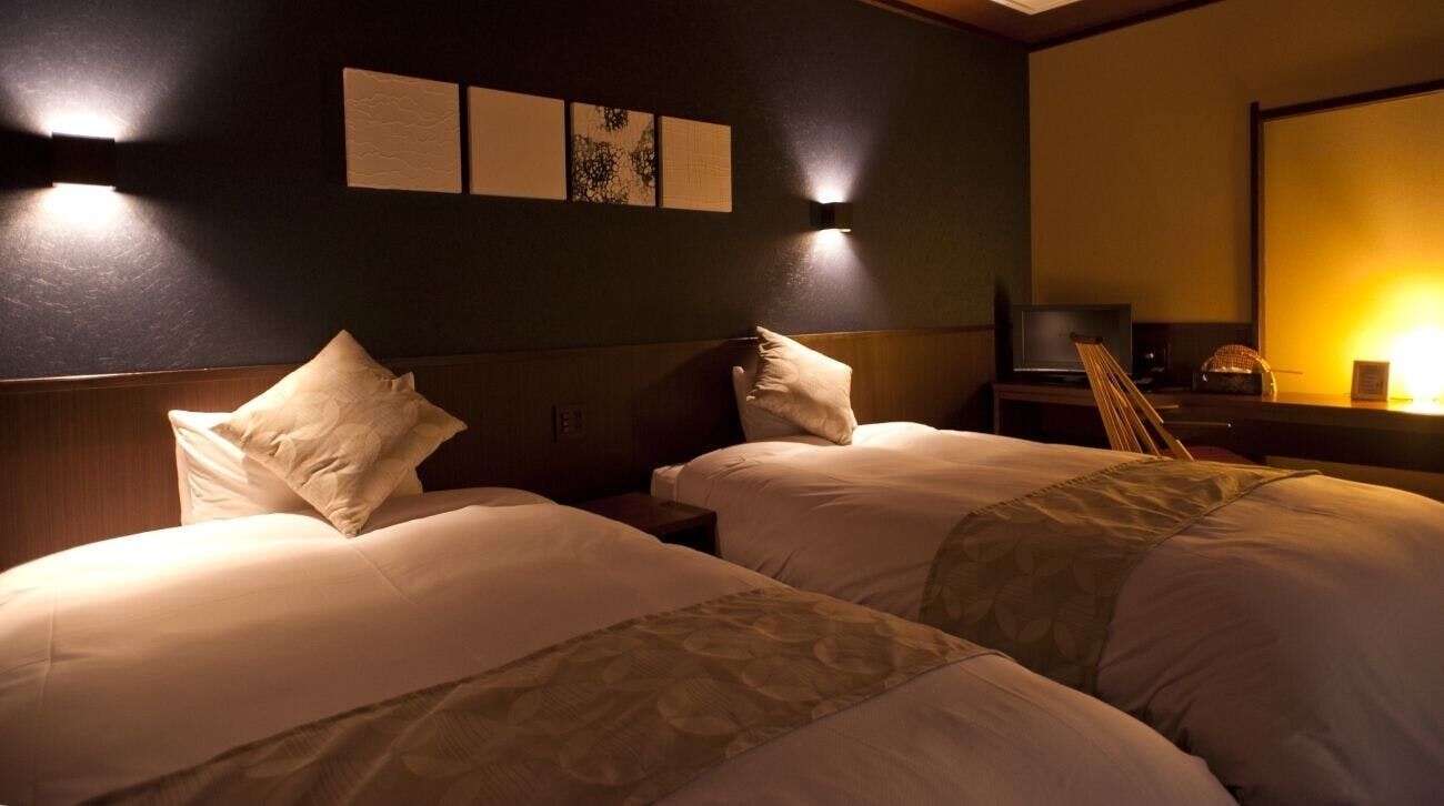 A hotel room with two beds, a desk with a chair, a flat-screen TV, and wall-mounted artwork.