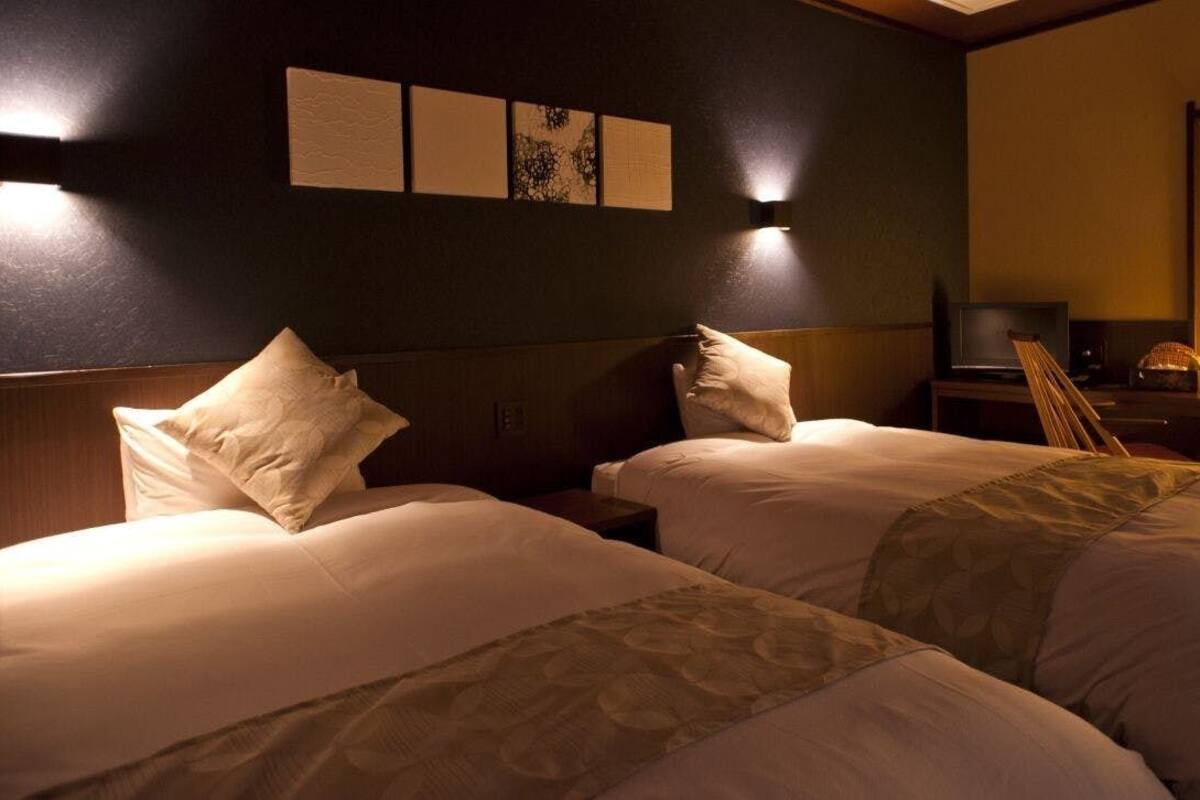 Une chambre d’hôtel avec deux lits, un bureau avec une chaise, un téléviseur à écran plat et des œuvres d’art accrochées au mur.