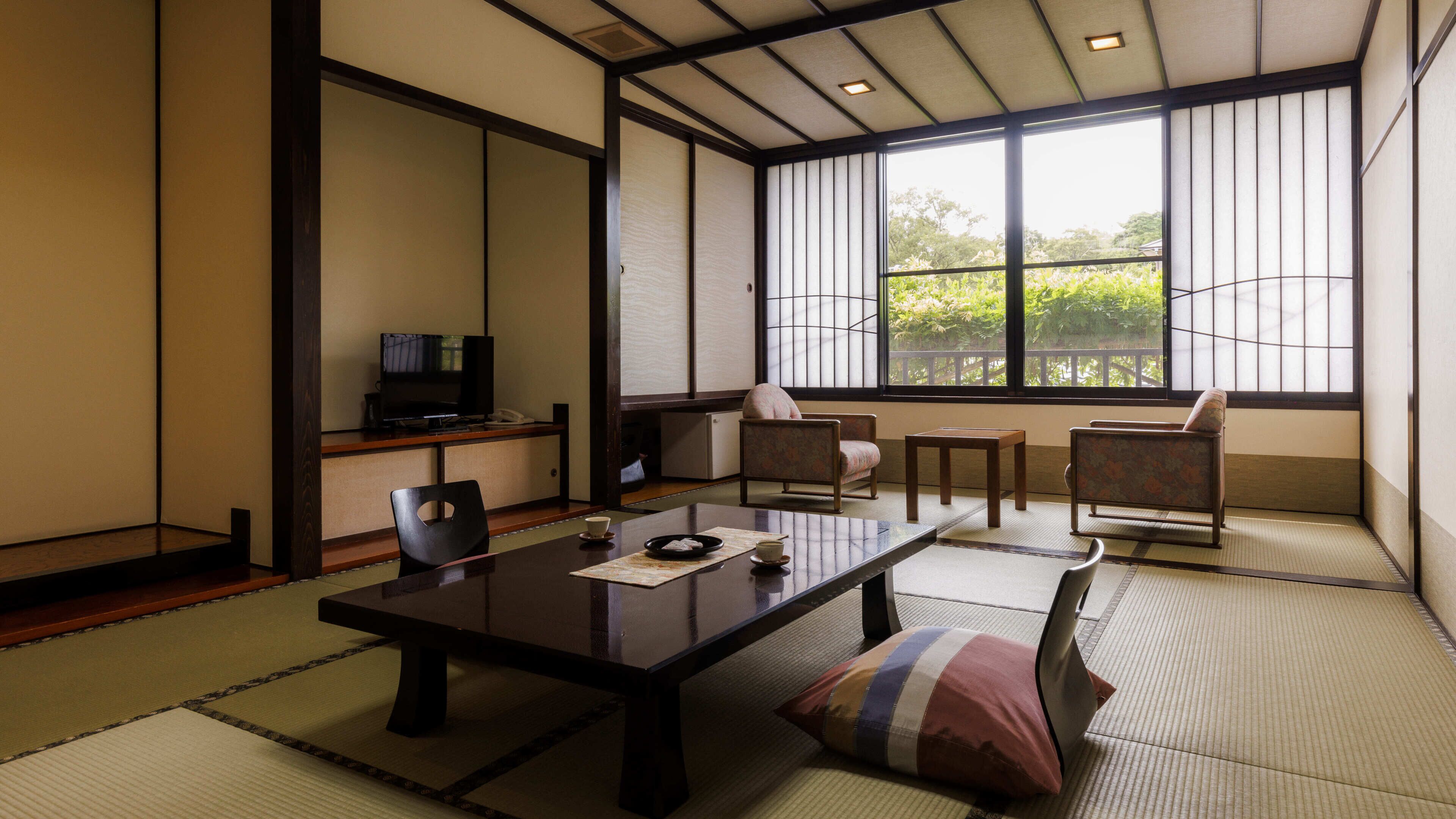 A traditional Japanese-style room with tatami flooring, a low table, chairs, a television, and a view of greenery outside.