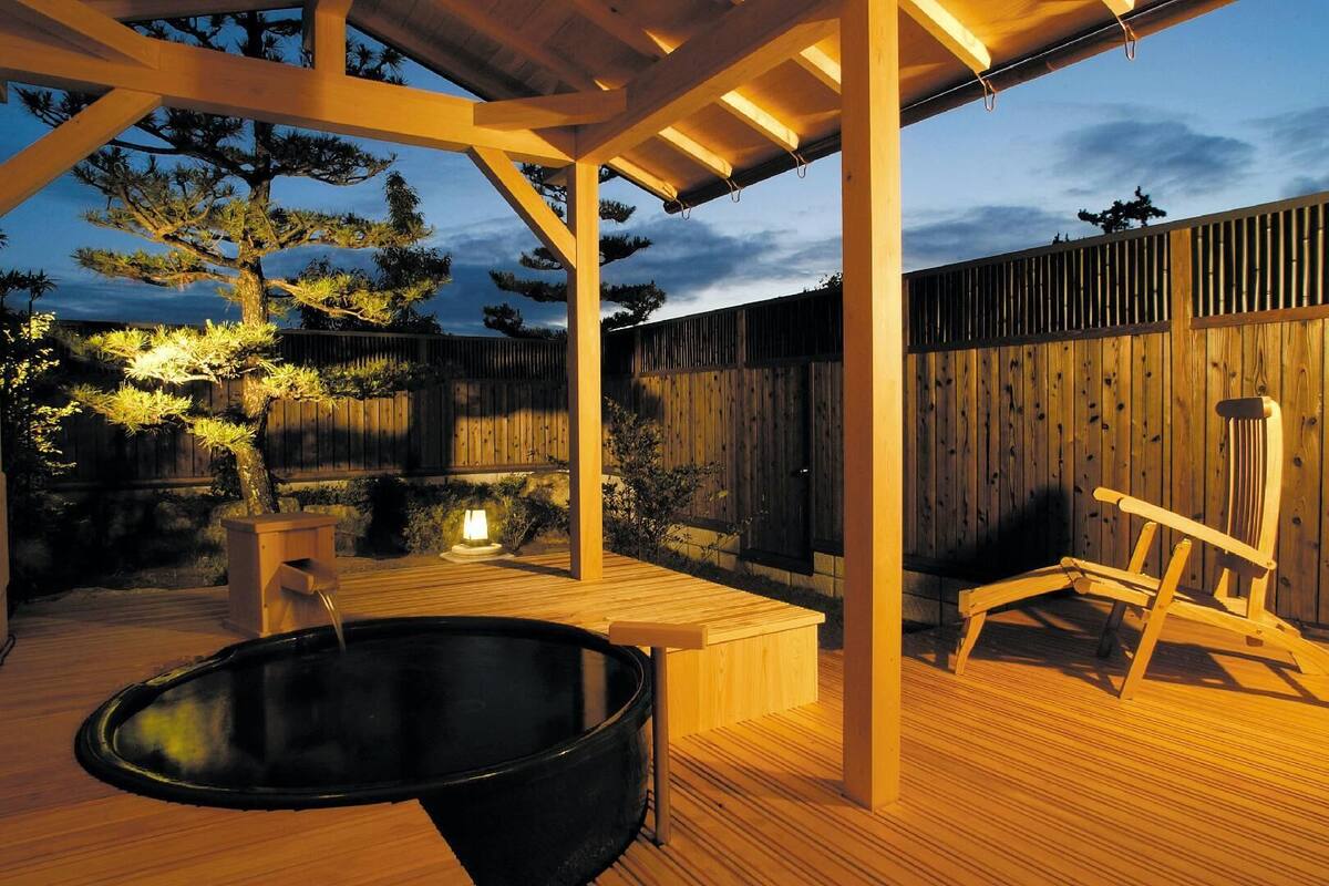 Une terrasse en bois avec un jacuzzi, une chaise en bois et une structure en forme de pergola.