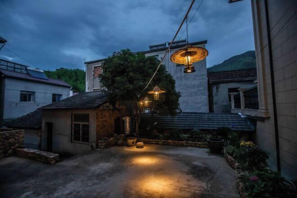 Une cour avec un mur en pierre, un petit bâtiment et des lampes suspendues.