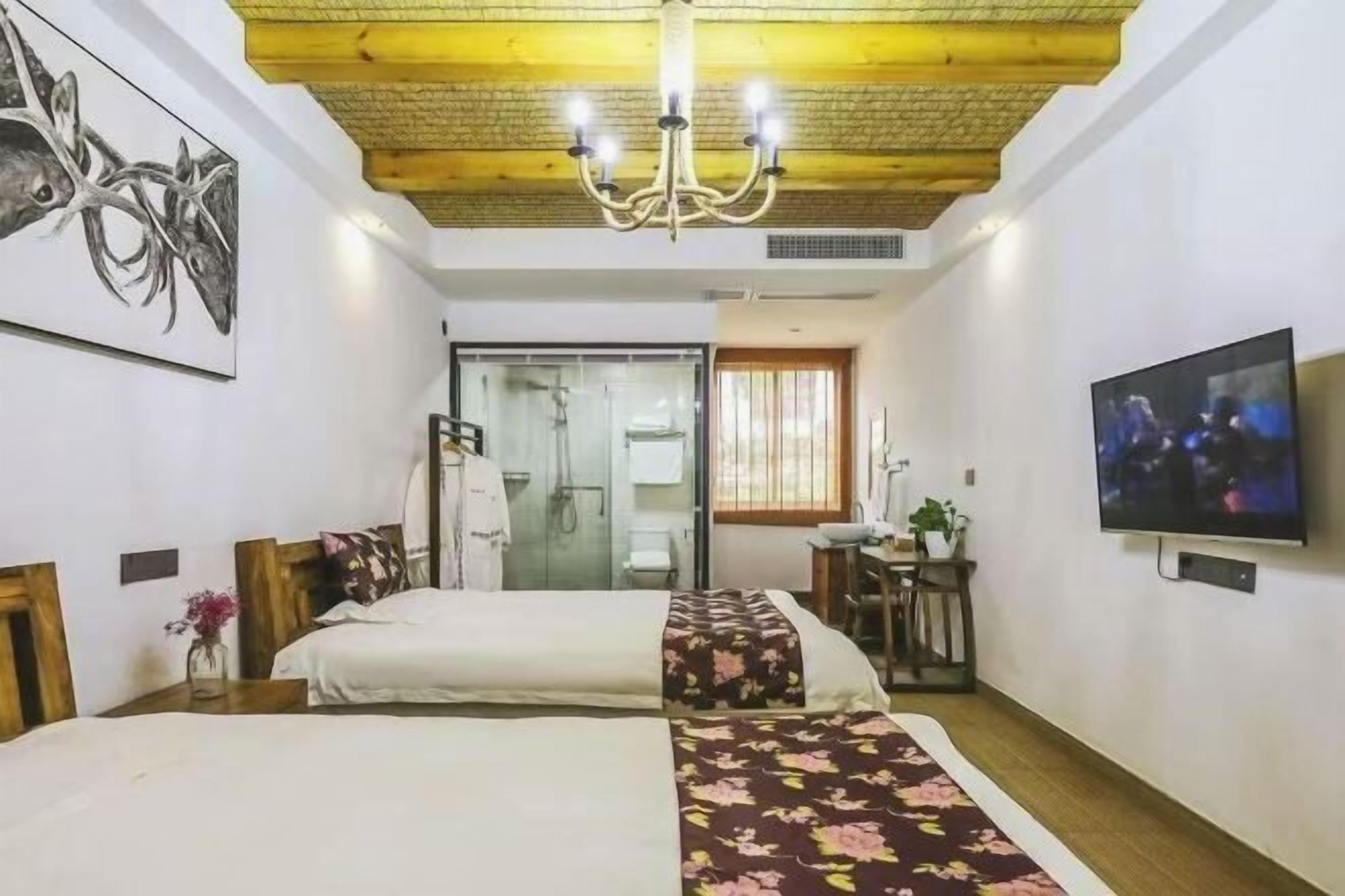 Habitación de hotel con dos camas, televisión, candelabro y zona de ducha.