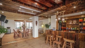 Un interior rústico con pisos de madera, una zona de bar con taburetes y un comedor con mesas y sillas.