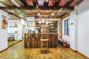 Un espace bar avec un comptoir en bois, des tabourets et une étagère remplie de bouteilles.