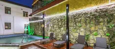 A poolside area with lounge chairs, a stone wall, and a balcony.