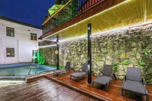 Ein Poolbereich mit Liegestühlen, einer Steinmauer und einem Balkon.