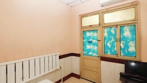 A room with a white radiator, a wooden door with blue-tinted glass panels, and a television on a stand.