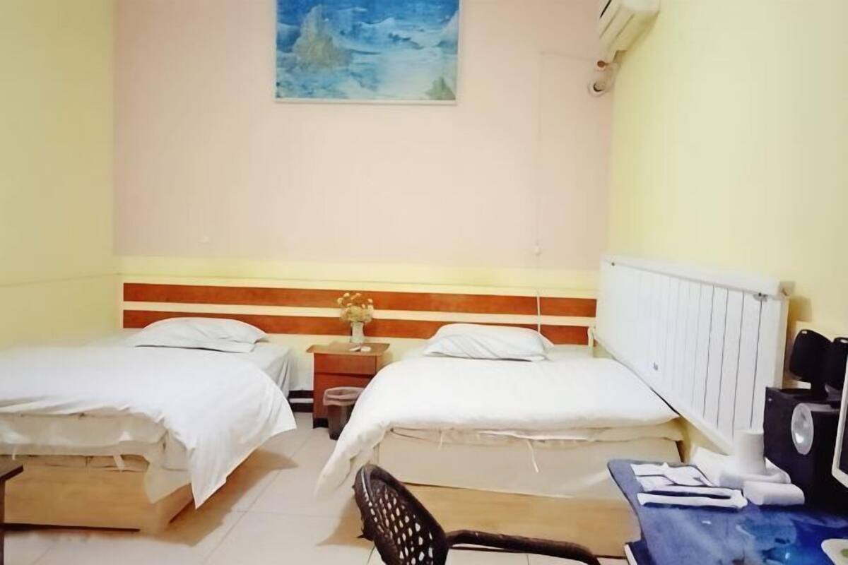 Una habitación con dos camas, una mesita de noche, una silla y un radiador.