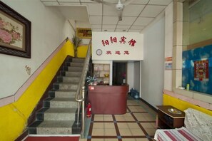 Un hall d’hôtel avec un comptoir d’accueil, un escalier et un lit au premier plan.